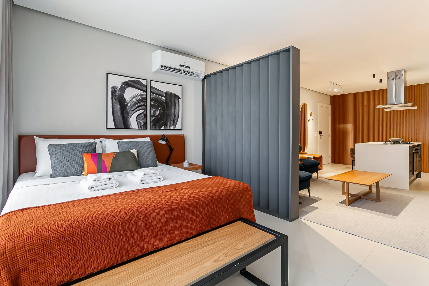 A bedroom with a bed beside a partition and an open kitchen area.