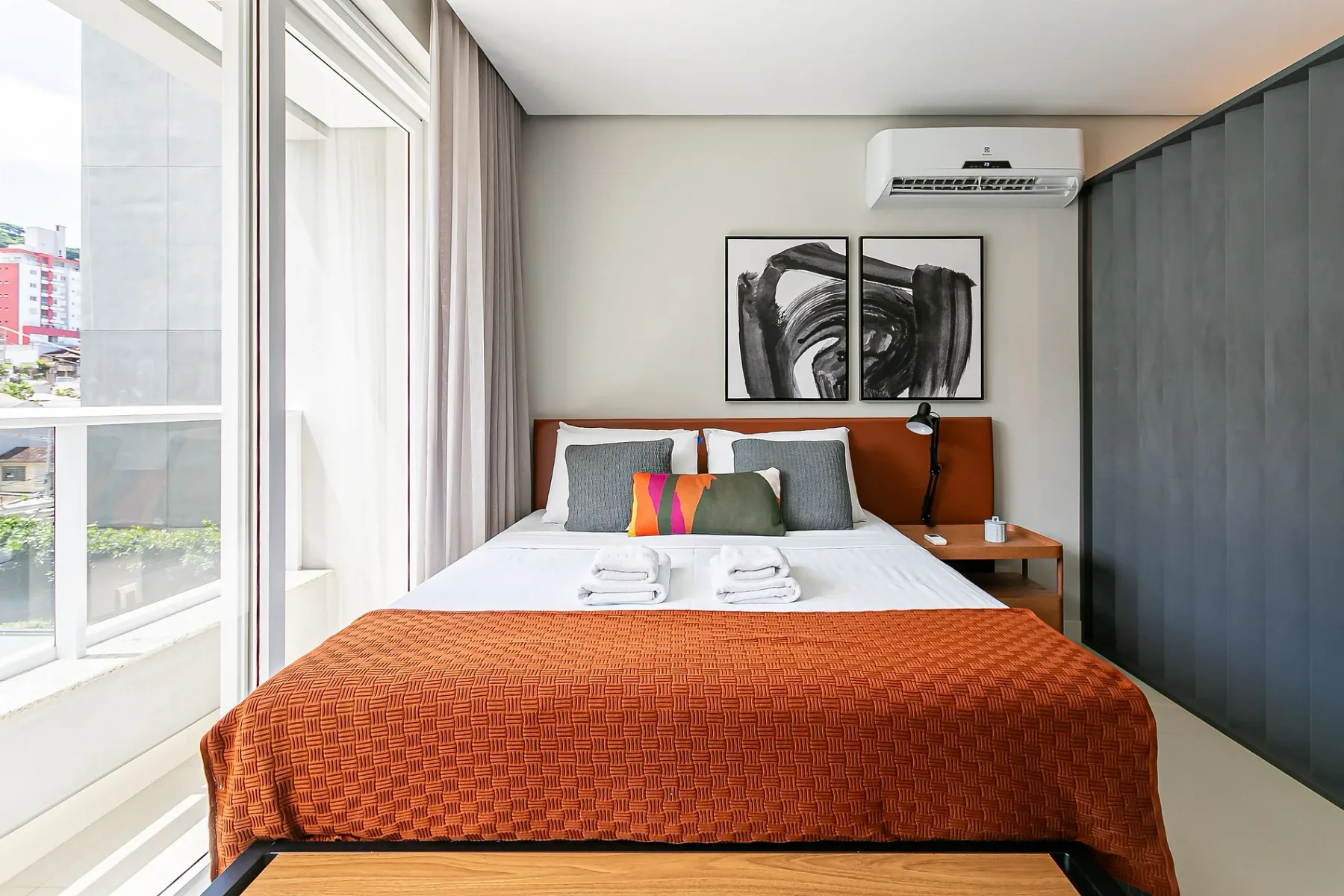 A bedroom with a bed, bedside table, and large windows.