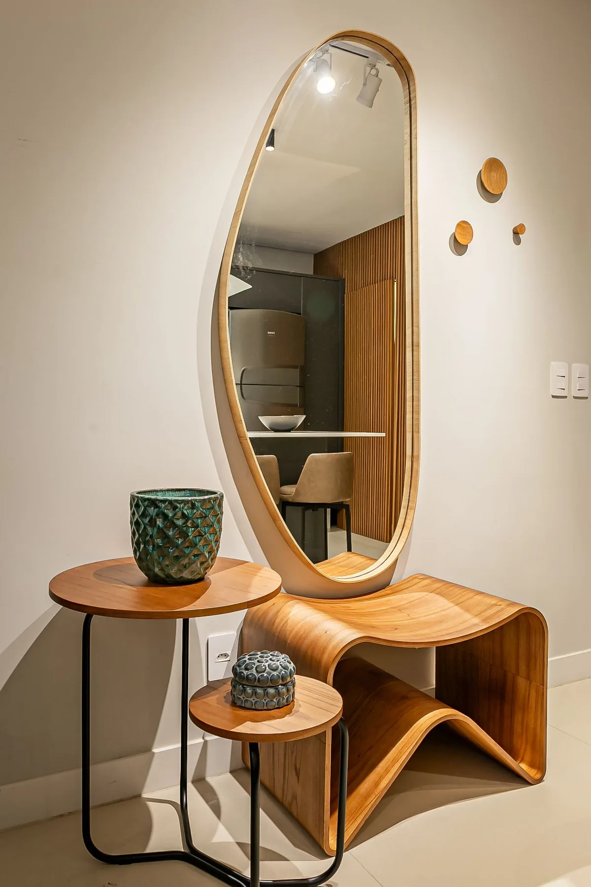 A full-length mirror stands above a curved wooden console in a bright interior.