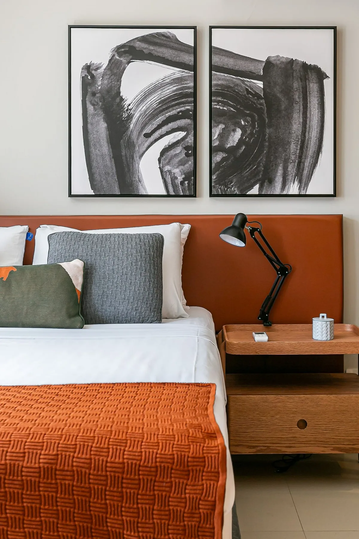 A bedroom with a neatly made bed, framed artwork, and a bedside table.