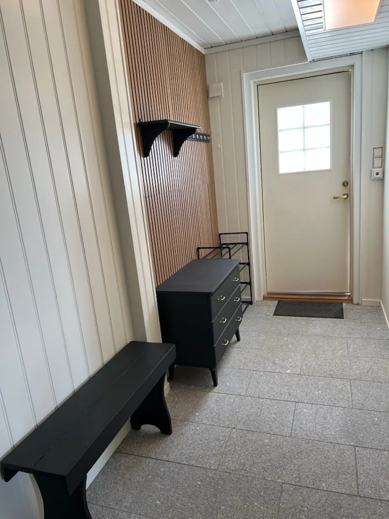 Una entrada con suelo de baldosas, un banco, una cómoda y una puerta con ventana.