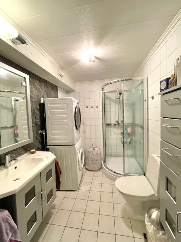 Un baño alicatado con ducha, inodoro, lavabo y máquinas de lavar apiladas.