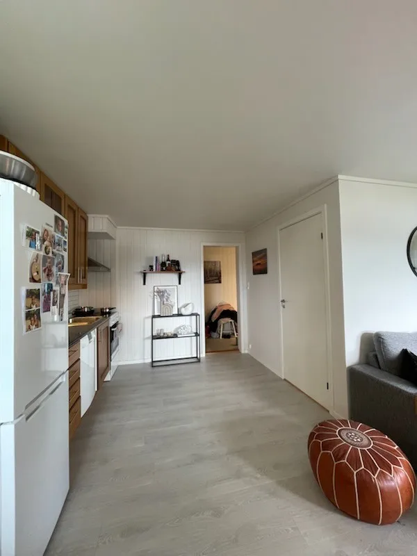 Una cocina compacta se abre a una sala con un sofá gris y un puf redondo.