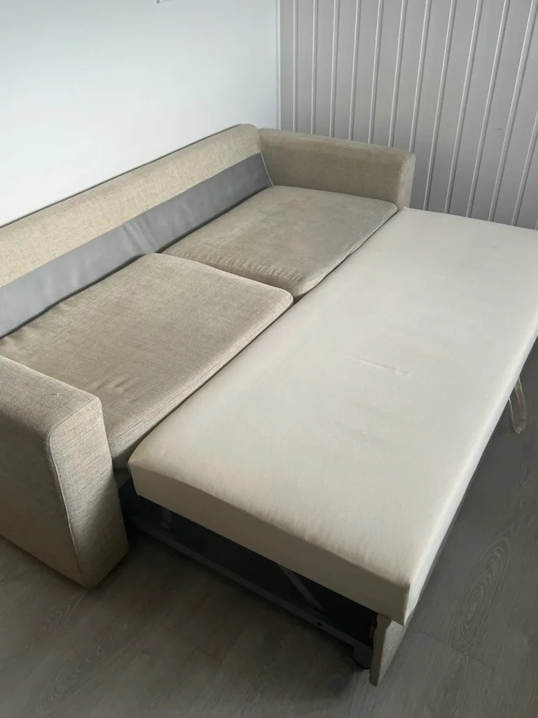 Un sofá seccional beige con una chaise longue extendida está junto a una pared panelada.