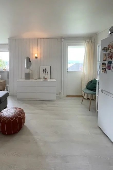 Una habitación luminosa con una cómoda blanca, ventanas y una silla verde.
