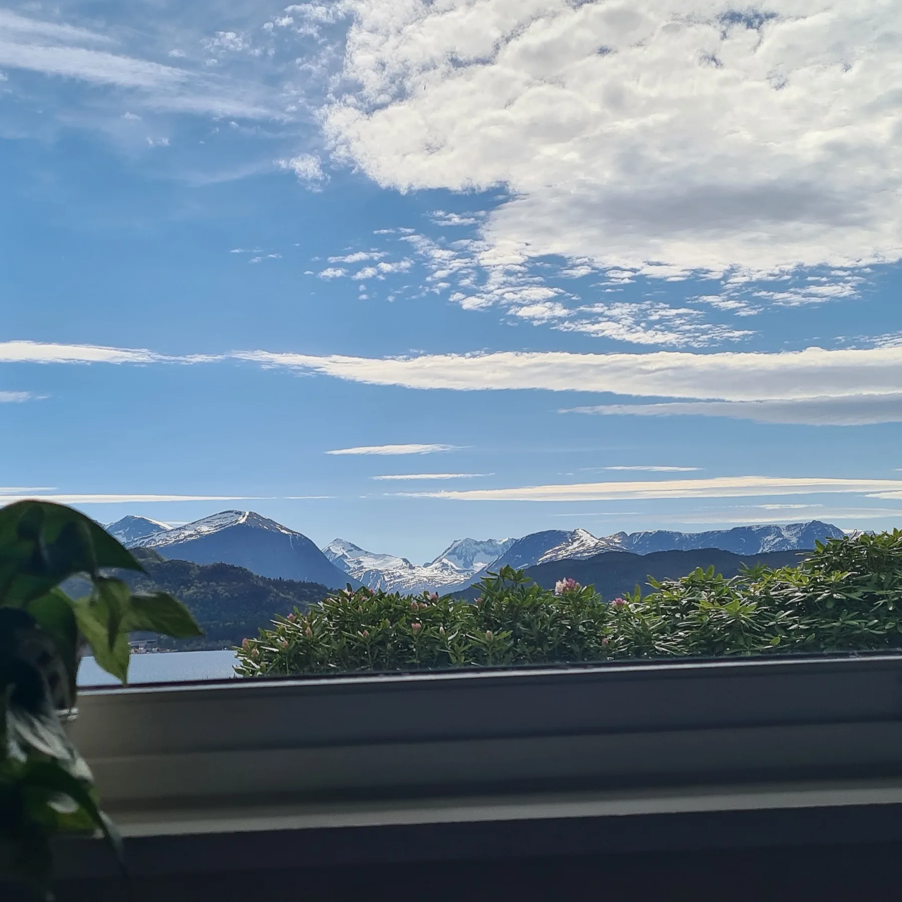 Se ve un paisaje montañoso más allá de una ventana, bajo un cielo azul con nubes.