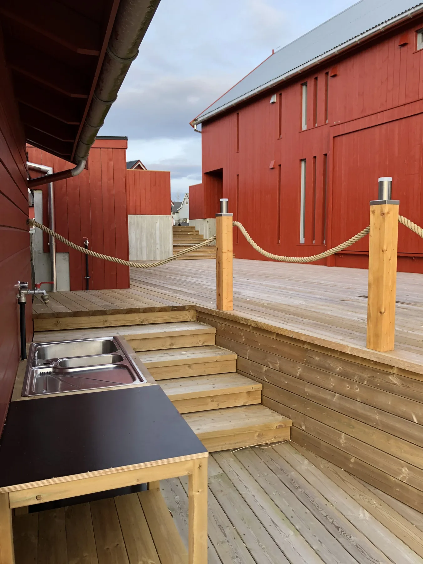 Zona común: Una terraza exterior de madera con escalones y una zona de cocina integrada entre edificios rojos.