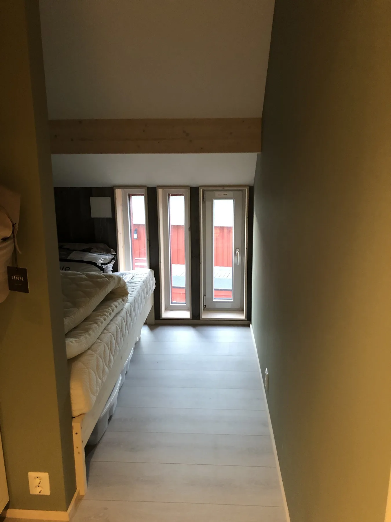 Un dormitorio estrecho con una cama junto a ventanas altas.
