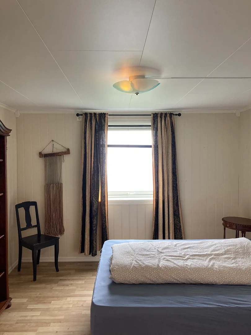 Un dormitorio con una cama junto a una ventana enmarcada por cortinas.