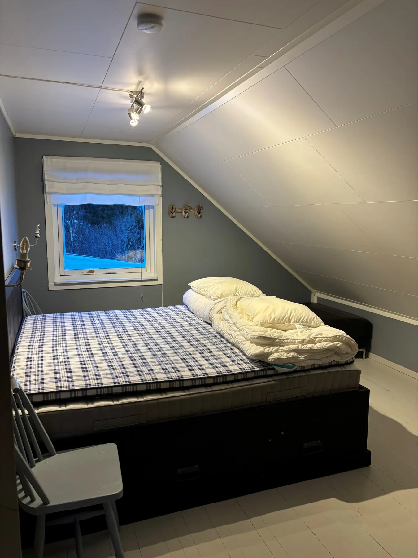 Un dormitorio con una cama bajo un techo inclinado y una ventana.
