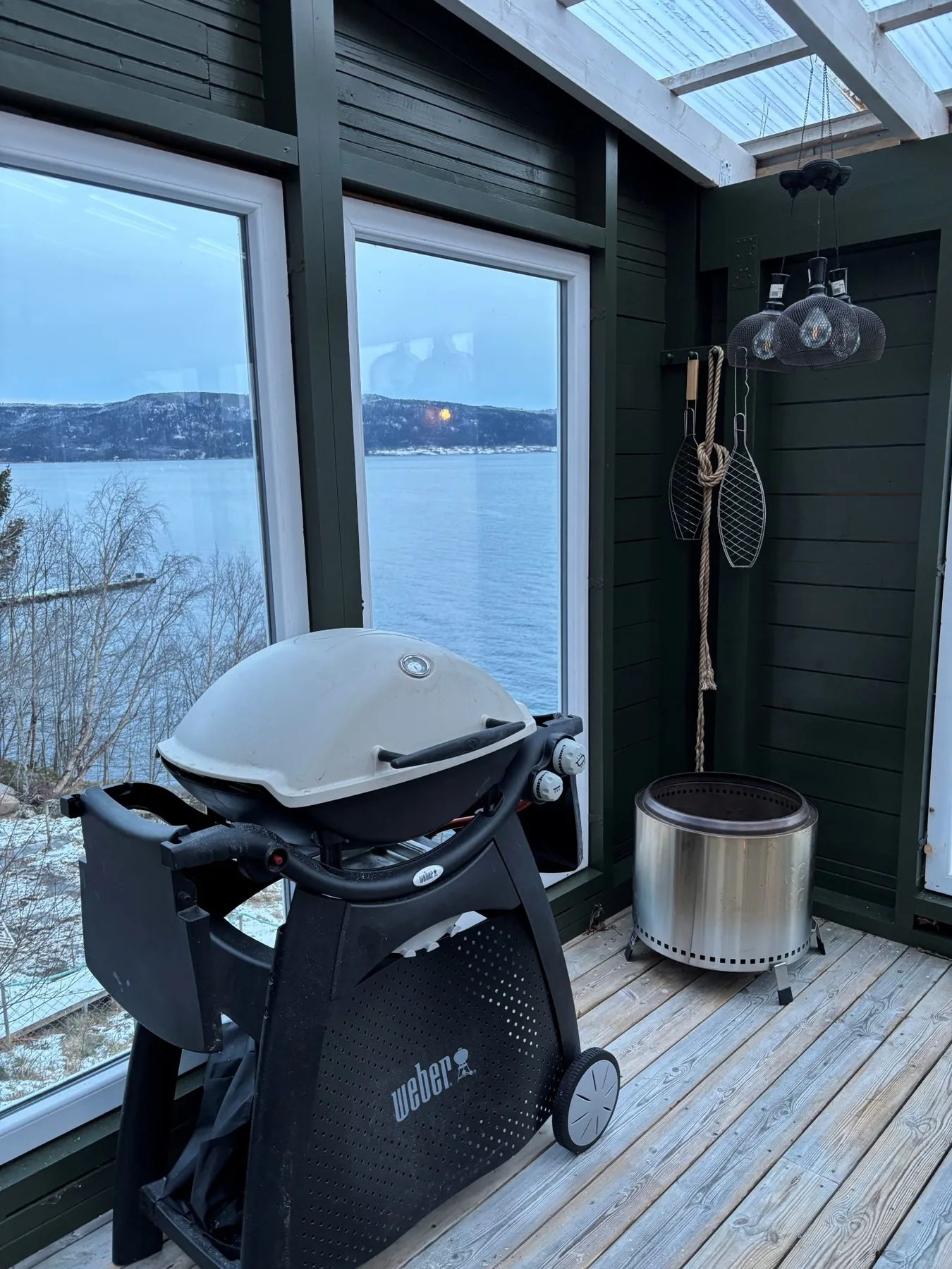 Una terraza exterior cubierta con una parrilla y vistas a un paisaje nevado junto al lago.