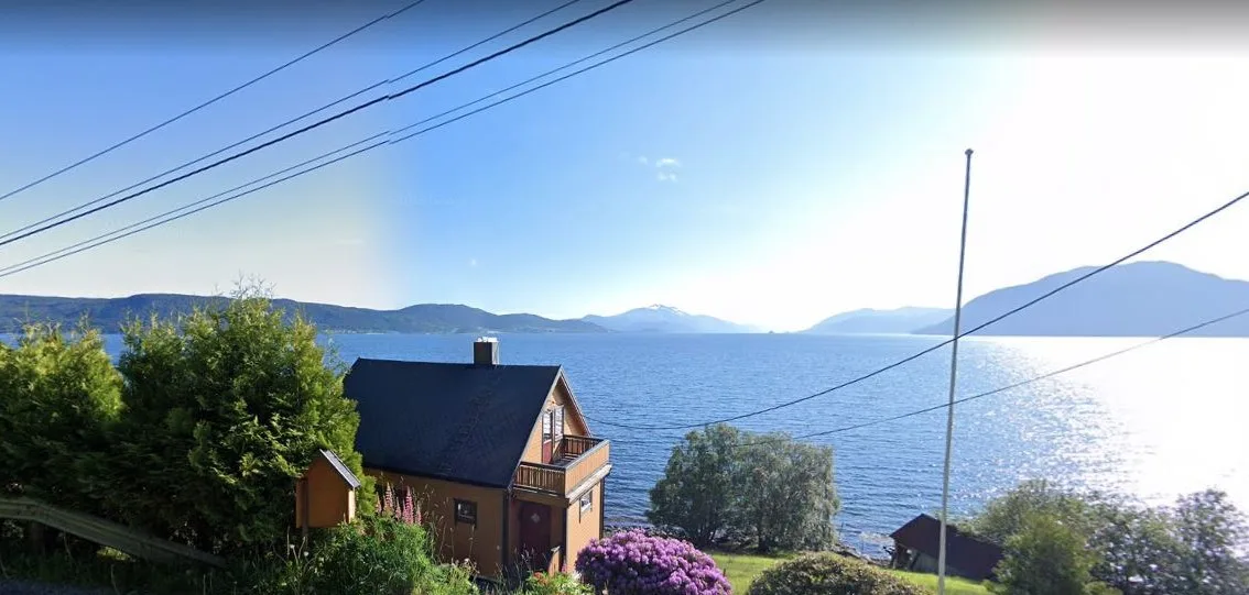 Una casa junto al lago y un jardín miran al agua y a montañas lejanas.