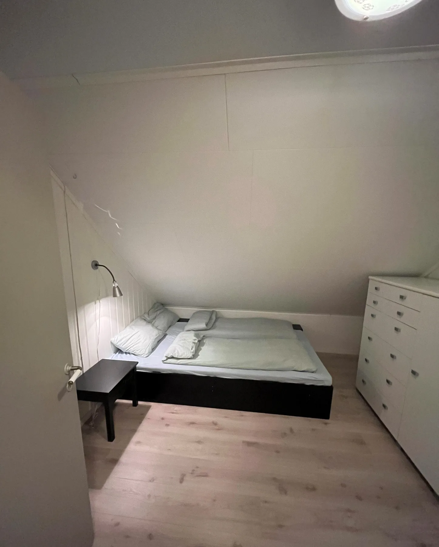 Un dormitorio abuhardillado compacto con una cama baja, una mesita y una cómoda.