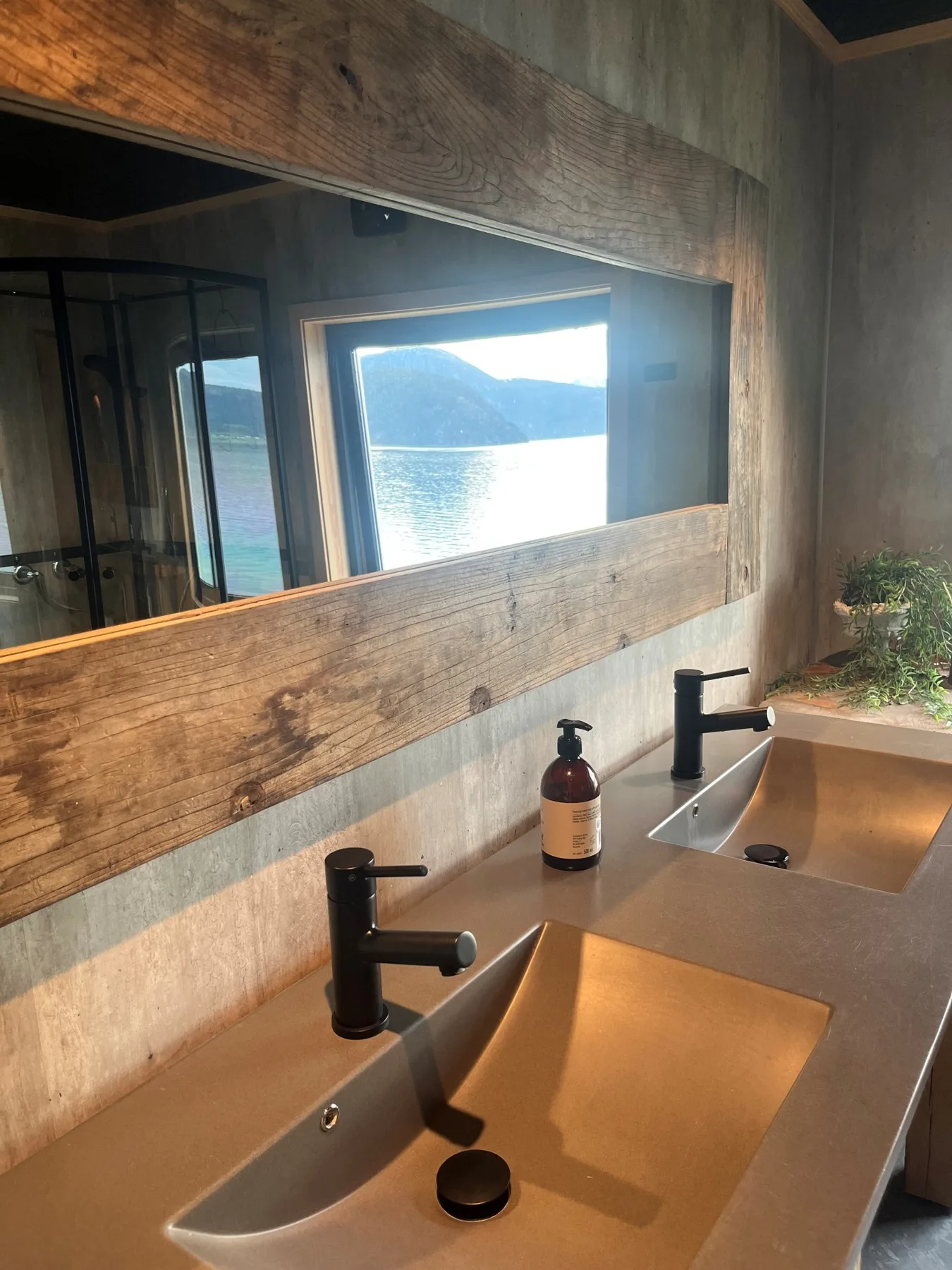 Un mueble de baño con dos lavabos está bajo un espejo grande con vistas al agua.
