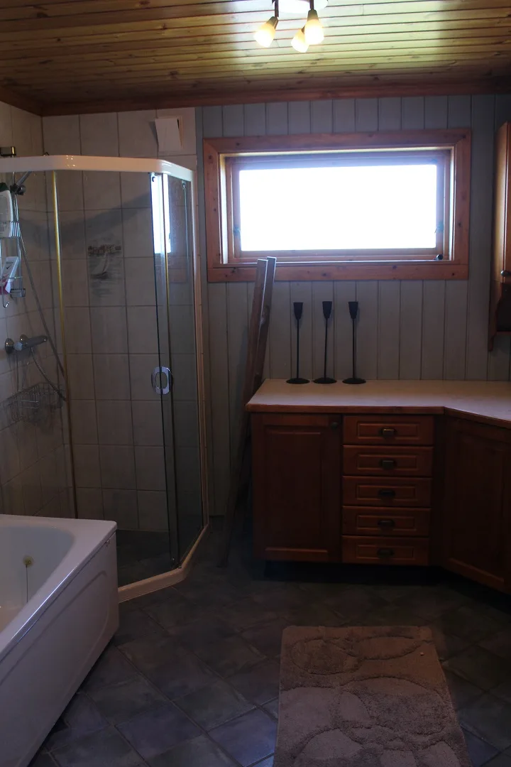 Un baño con ducha de vidrio, bañera y tocador de madera bajo una ventana.
