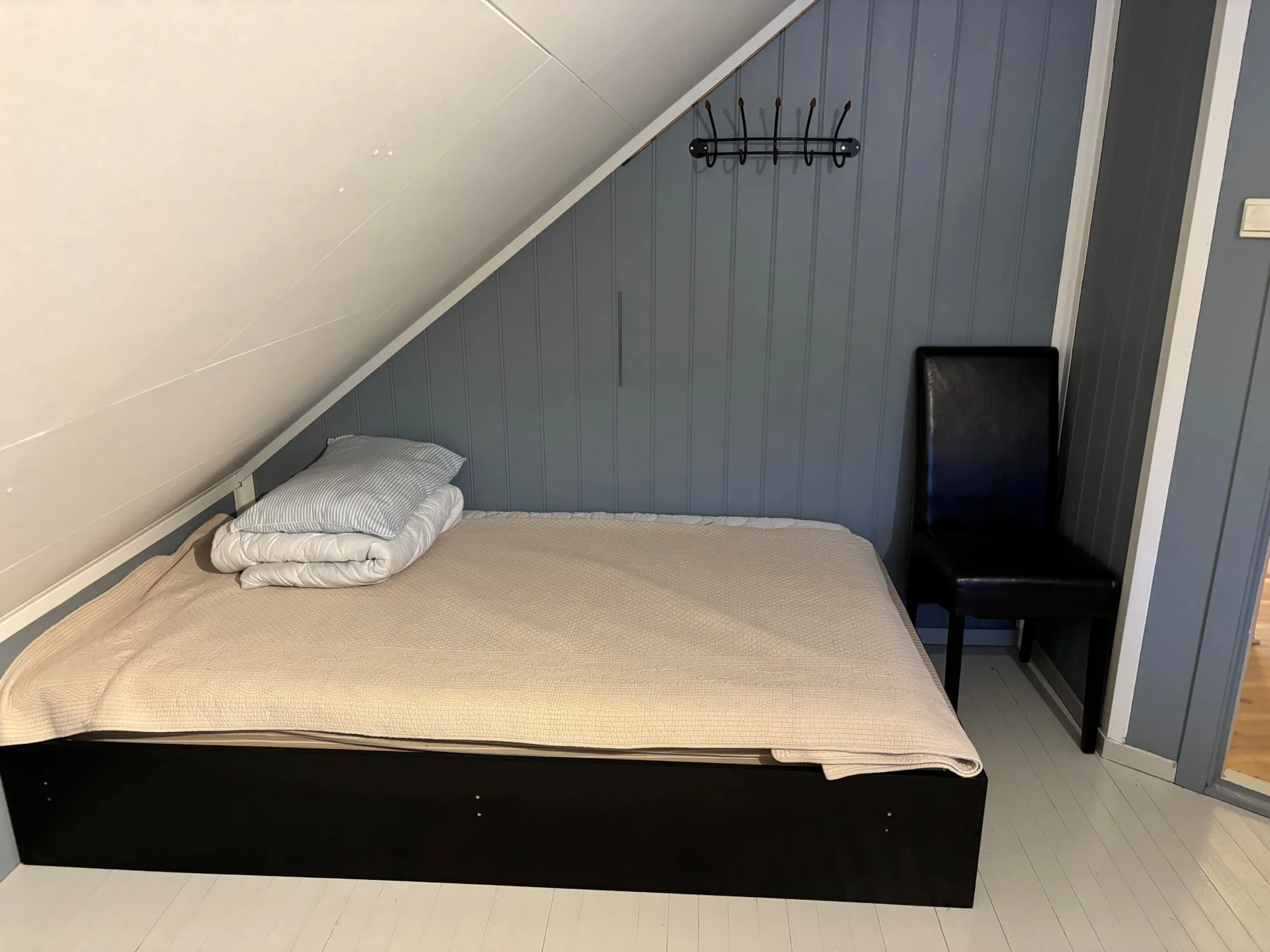 Una zona para dormir con una cama baja, ropa de cama doblada y una silla.
