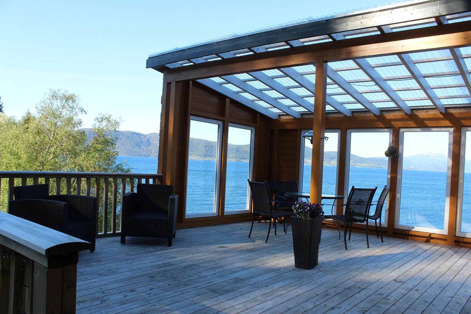 Una terraza exterior cubierta con asientos ofrece vistas a un lago y colinas.