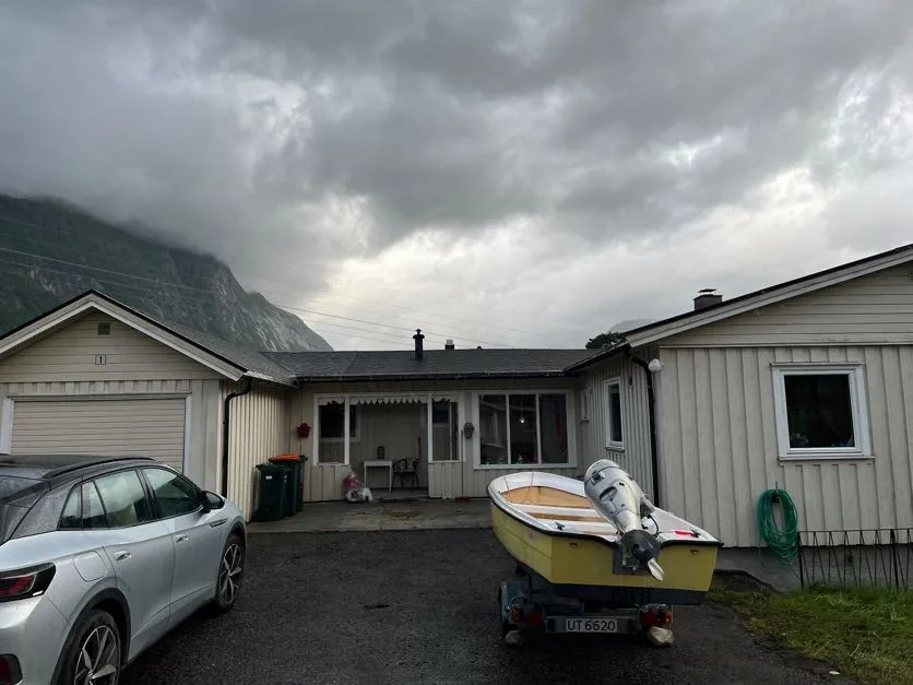 Una casa de una planta con un automóvil y un bote estacionados en la entrada, bajo un cielo nublado.