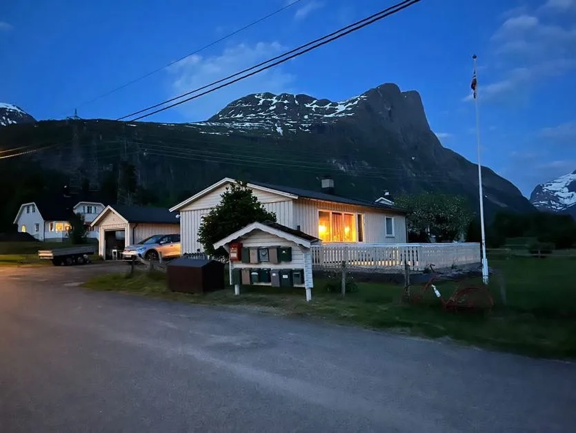 Un edificio pequeño con una ventana iluminada se encuentra al pie de una montaña al anochecer.