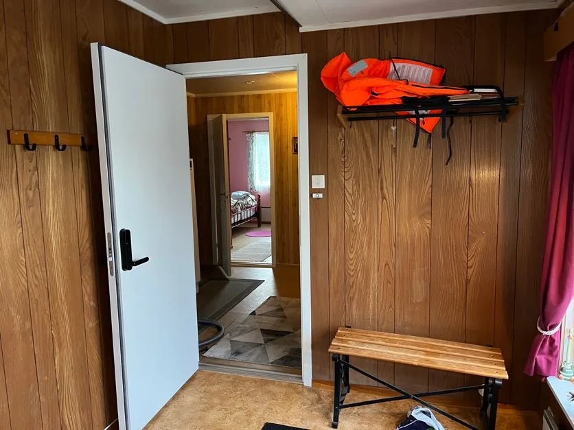 Un recibidor revestido de madera tiene una puerta blanca abierta y un banco.