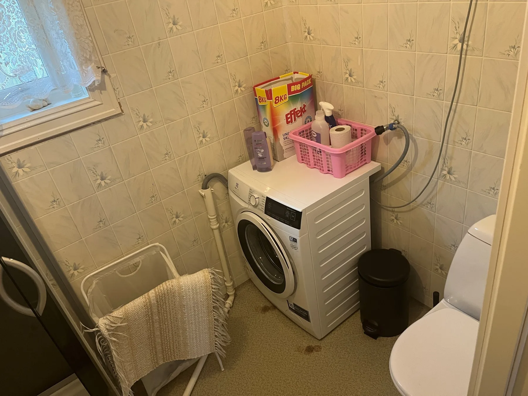 Una pequeña zona de lavandería con una lavadora junto a un inodoro.
