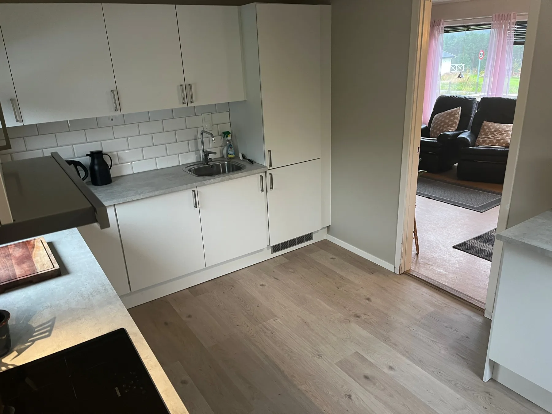 Una cocina con armarios blancos, una encimera y un fregadero da a una sala de estar.