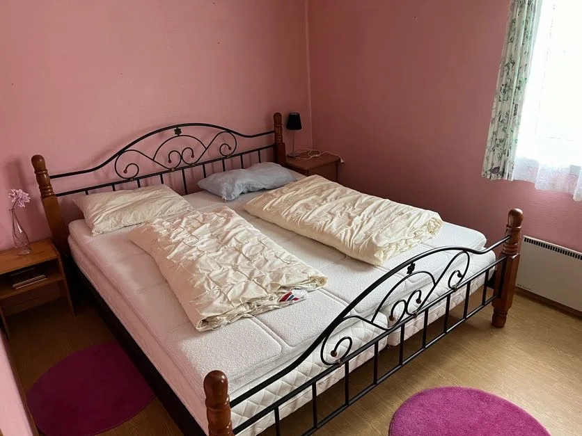 Un dormitorio con una cama doble, ropa de cama arrugada y una ventana con cortinas.