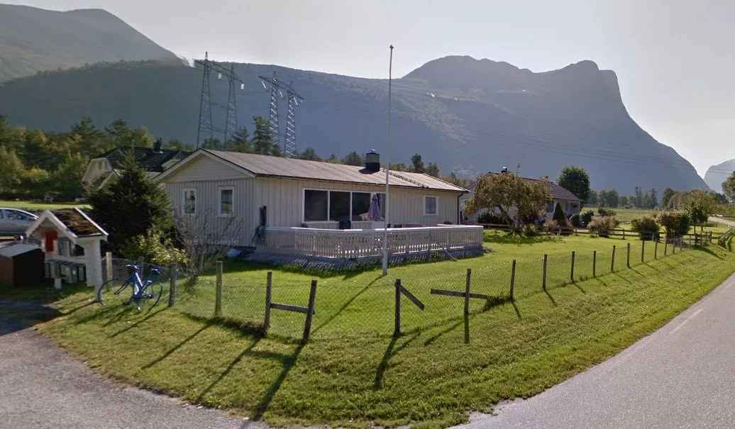 Una casa de una planta se encuentra junto a un jardín cubierto de césped y montañas.