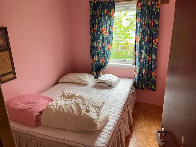 Un dormitorio con una cama bajo una ventana enmarcada por cortinas florales.
