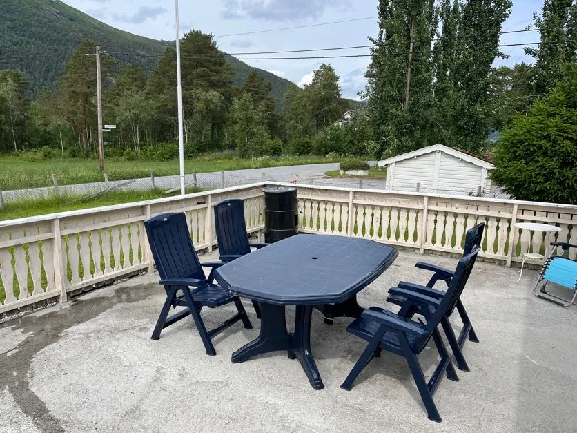 Un patio al aire libre tiene una mesa oscura y sillas junto a una barandilla.