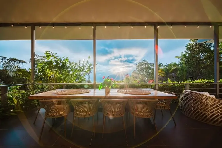 Un comedor exterior cubierto con una mesa larga y vegetación alrededor.
