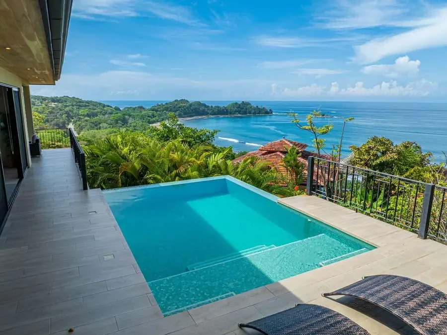 A pool overlooks lush coastal hills and the blue ocean.
