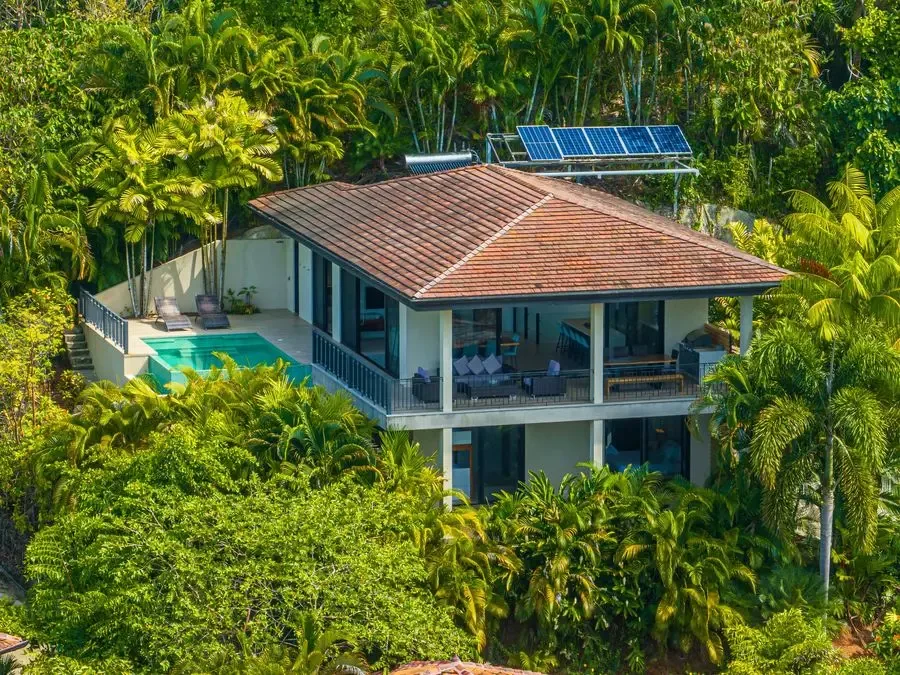 A house with a red-tiled roof sits among dense tropical greenery.