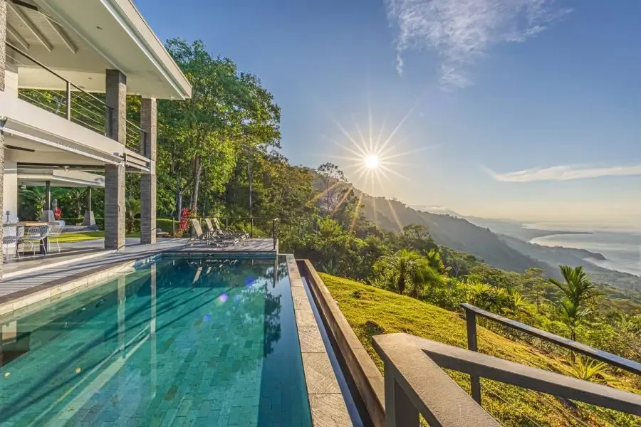 An outdoor pool beside a modern building overlooks a green mountain landscape.