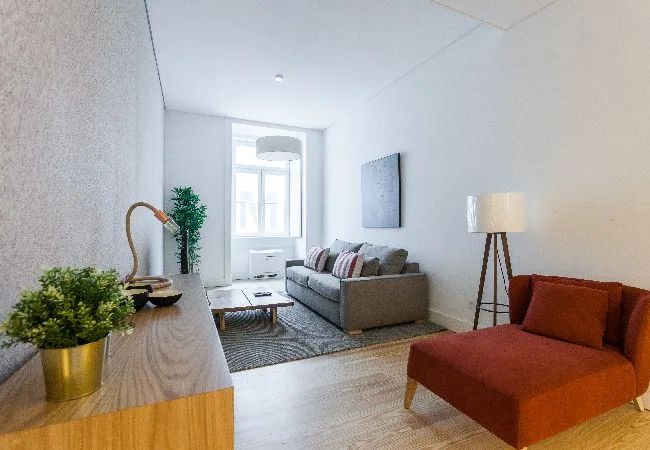 Una sala luminosa con un sofá gris y un sillón color óxido.