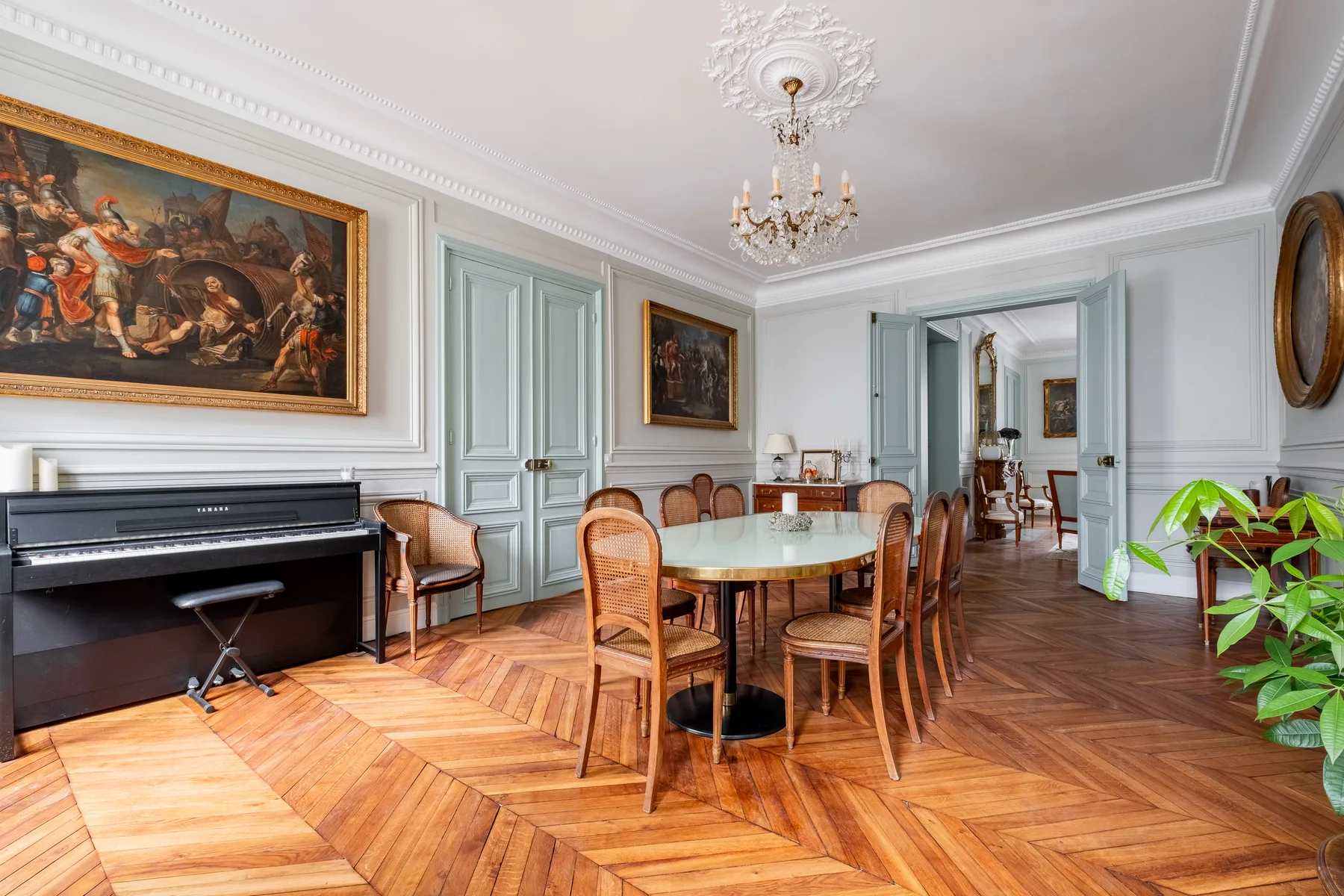 A formal dining room with a round table, wooden seating, and a piano.