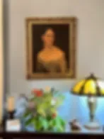 Espacio representativo del hotel: Un interior con luz tenue muestra un retrato enmarcado, plantas y una lámpara de mesa.
