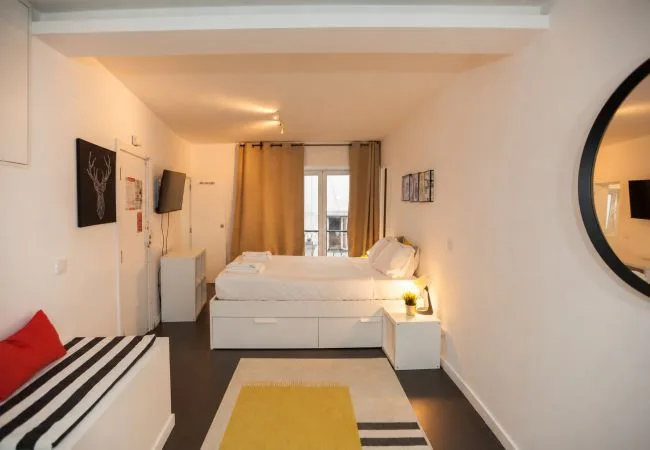 Un dormitorio con una cama, ventanas con cortinas y una pequeña zona de estar.