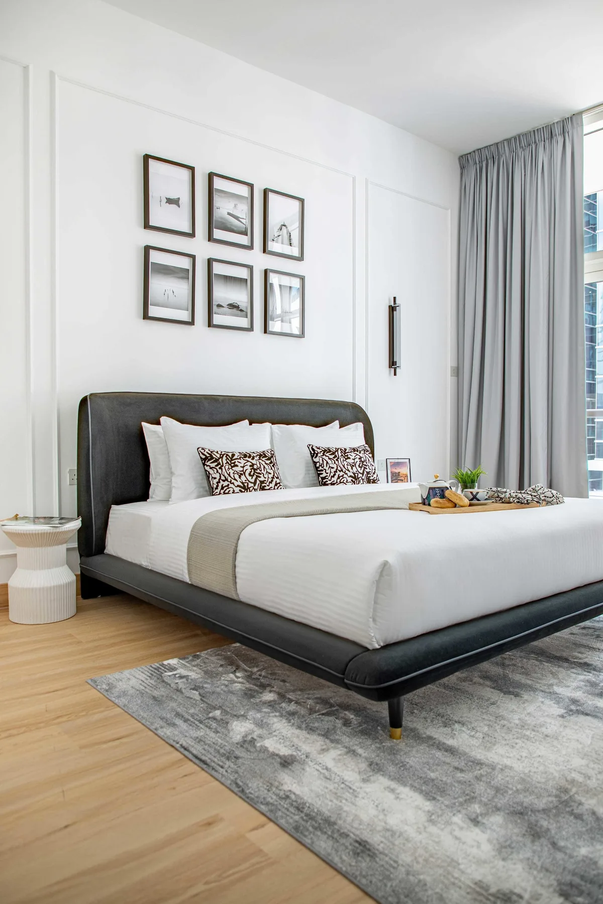 Un dormitorio luminoso con una cama grande, cuadros enmarcados y cortinas junto a la ventana.