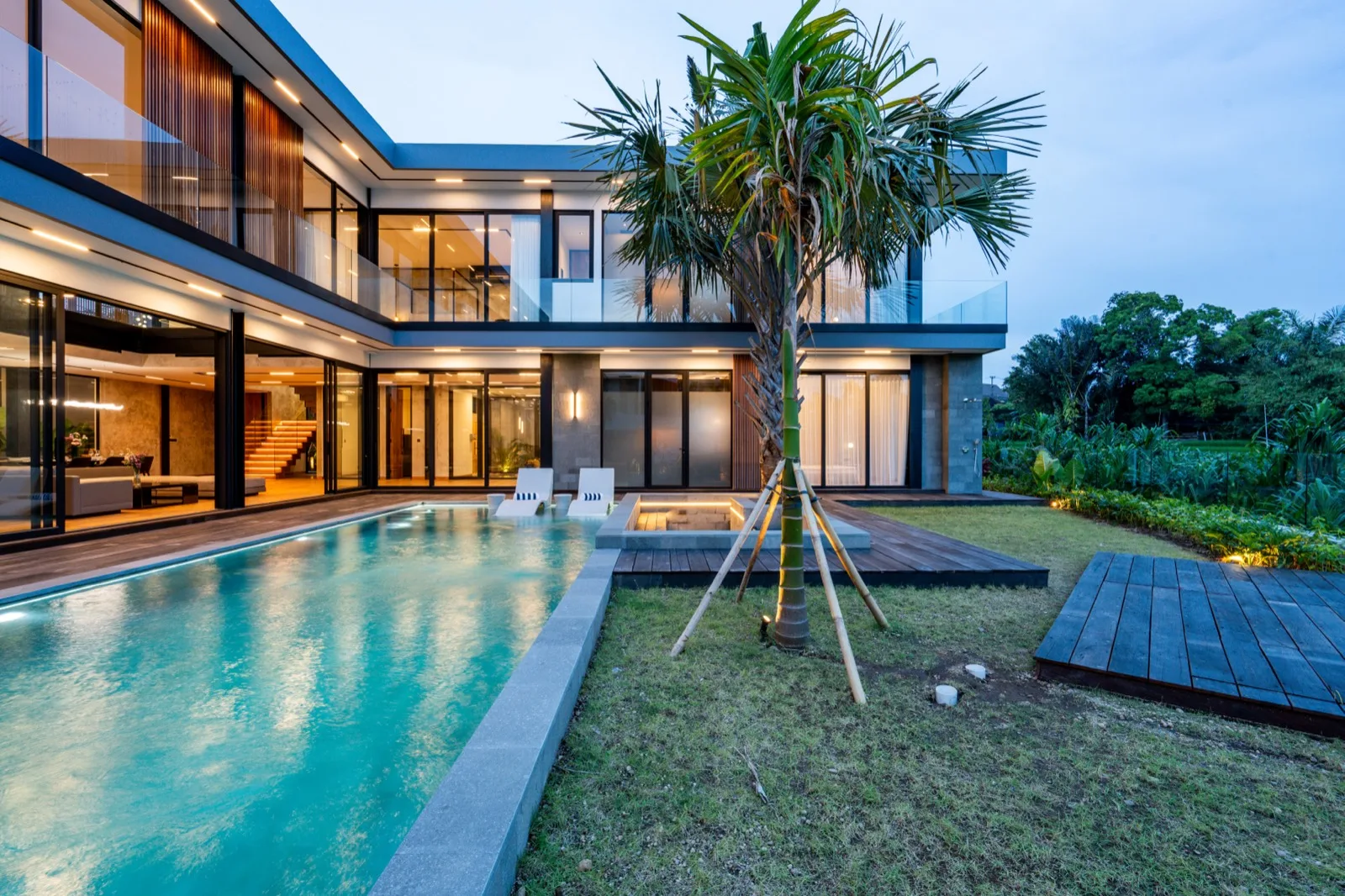 Una casa moderna junto a una piscina, con una palmera en el patio.