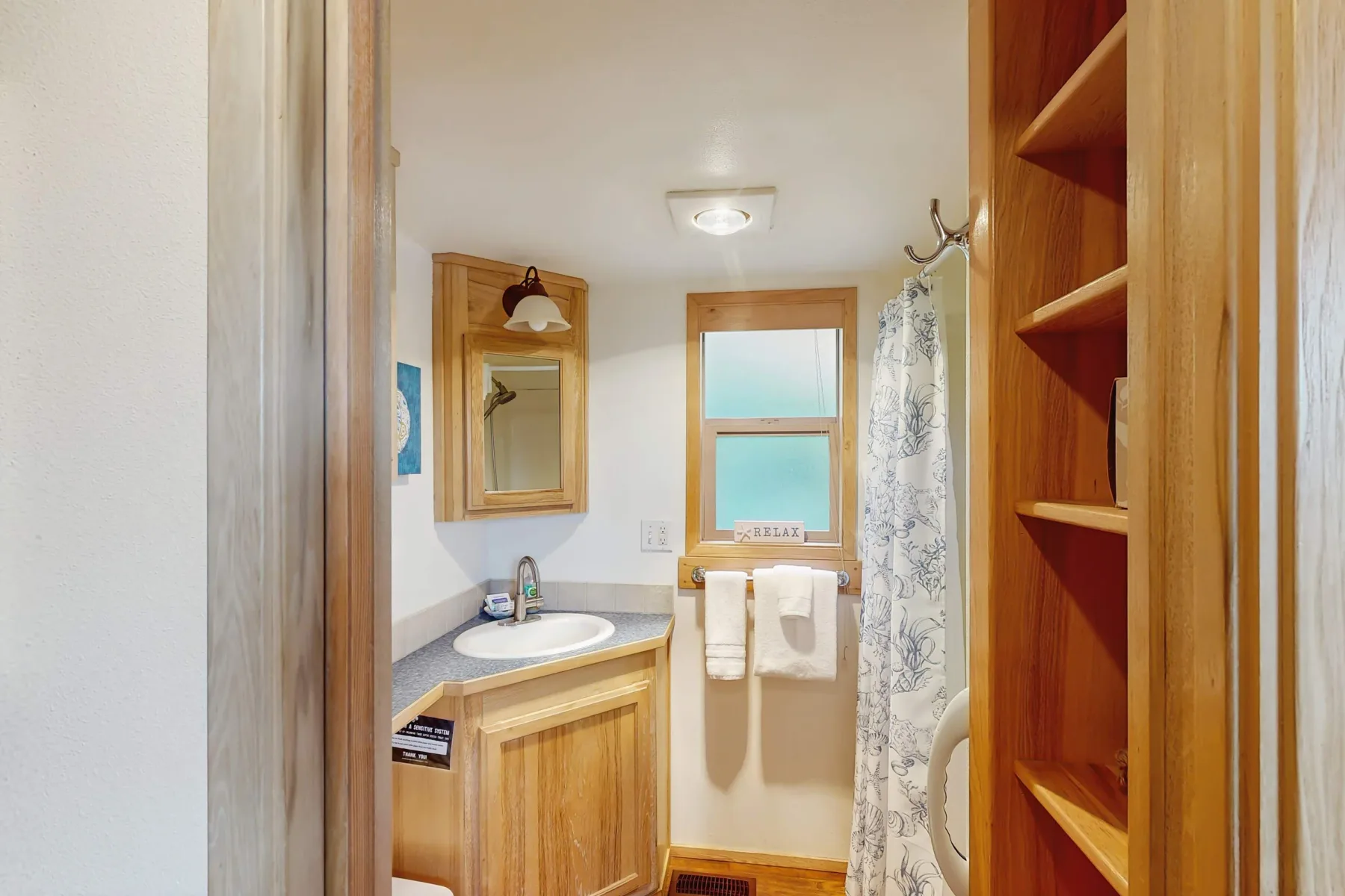 Un baño compacto con tocador, espejo y cortina de ducha junto a una ventana.