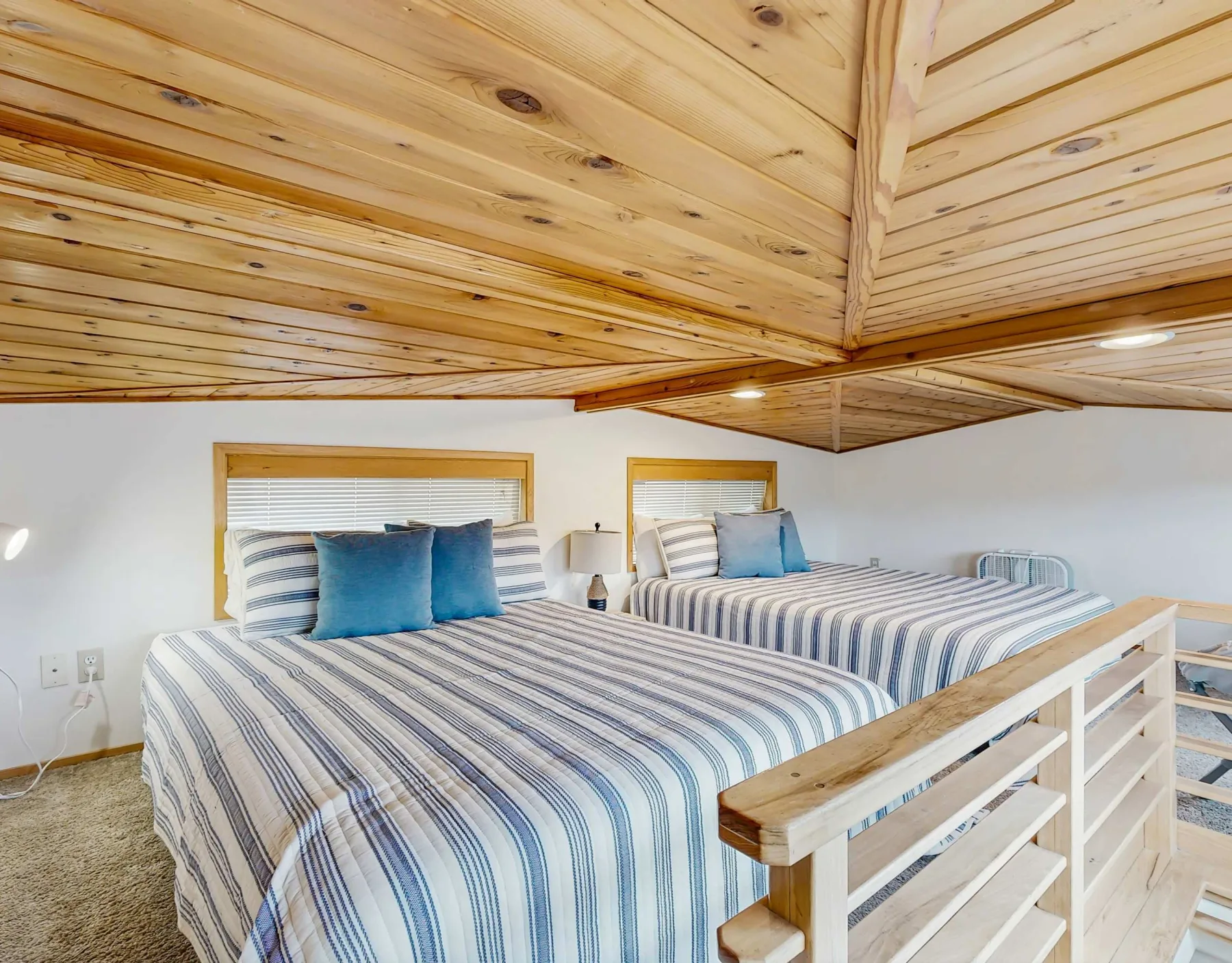 Un dormitorio con dos camas vestidas con ropa de rayas azules y blancas bajo un techo revestido de madera.