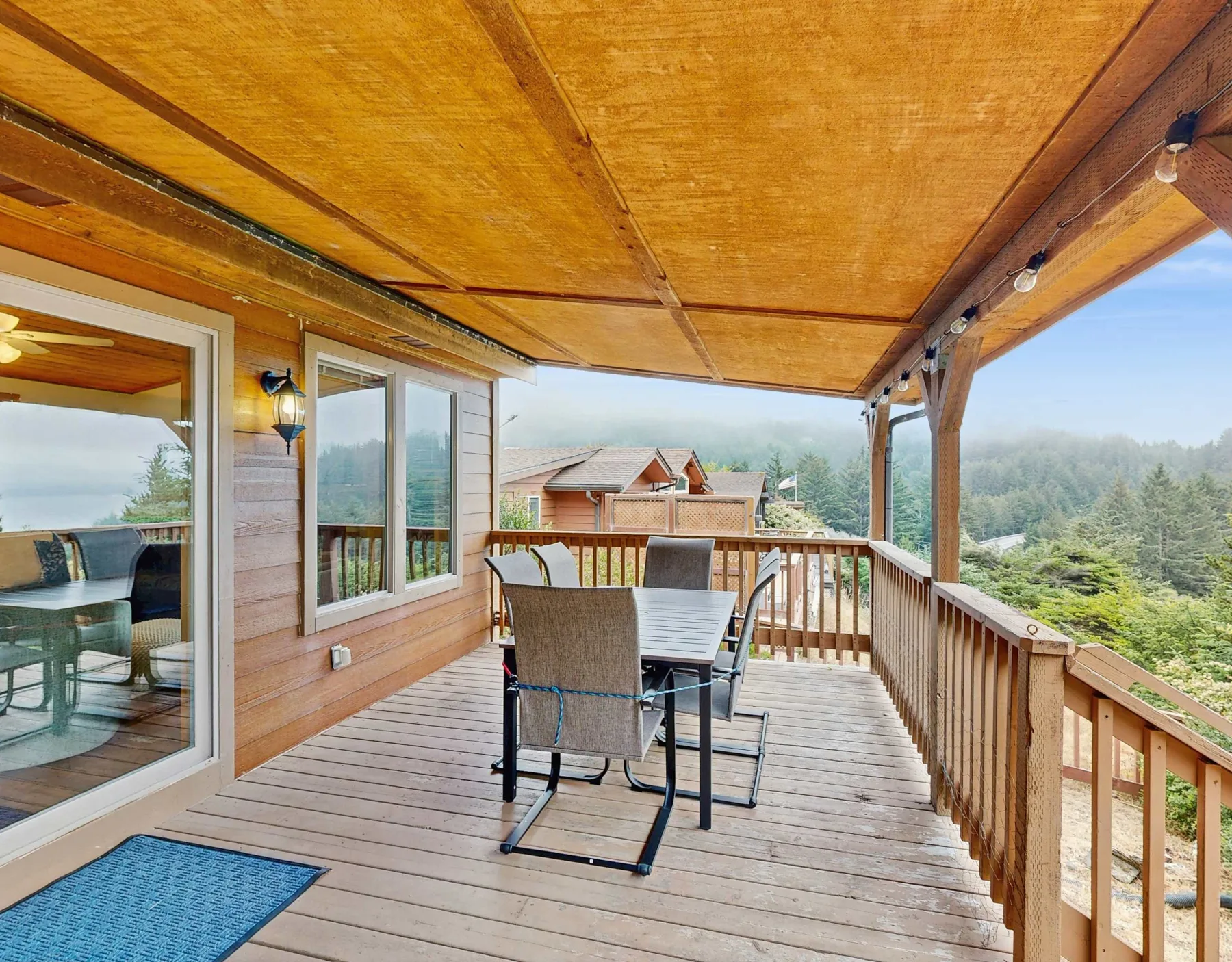 Una terraza de madera cubierta tiene una mesa de comedor y asientos con vista a los árboles.