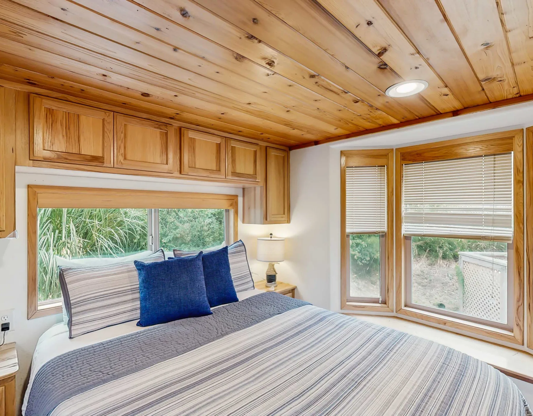 Dormitorio con una colcha a rayas, un cojín azul y techo de madera.