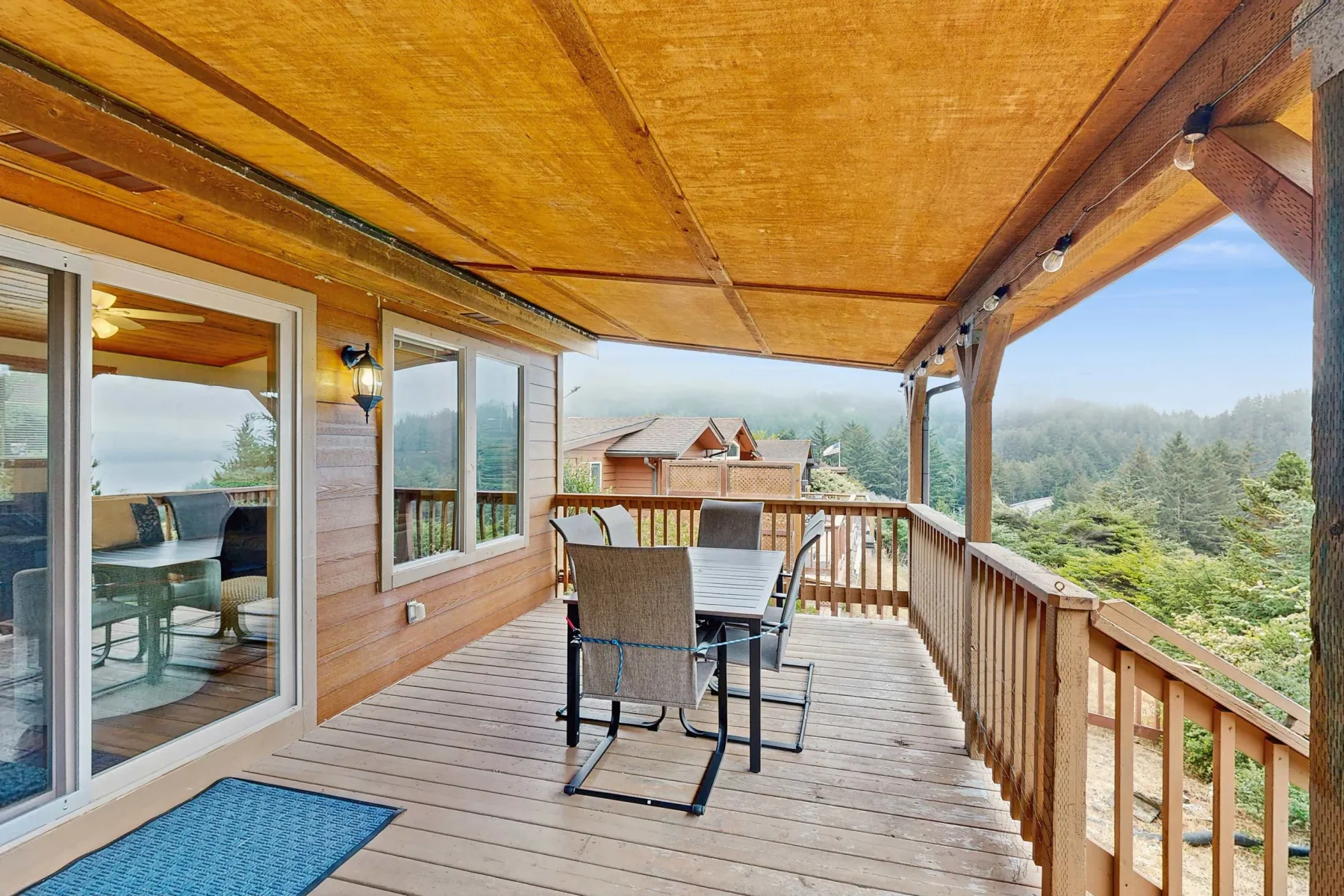 Una terraza de madera cubierta con asientos al aire libre da a un paisaje boscoso.
