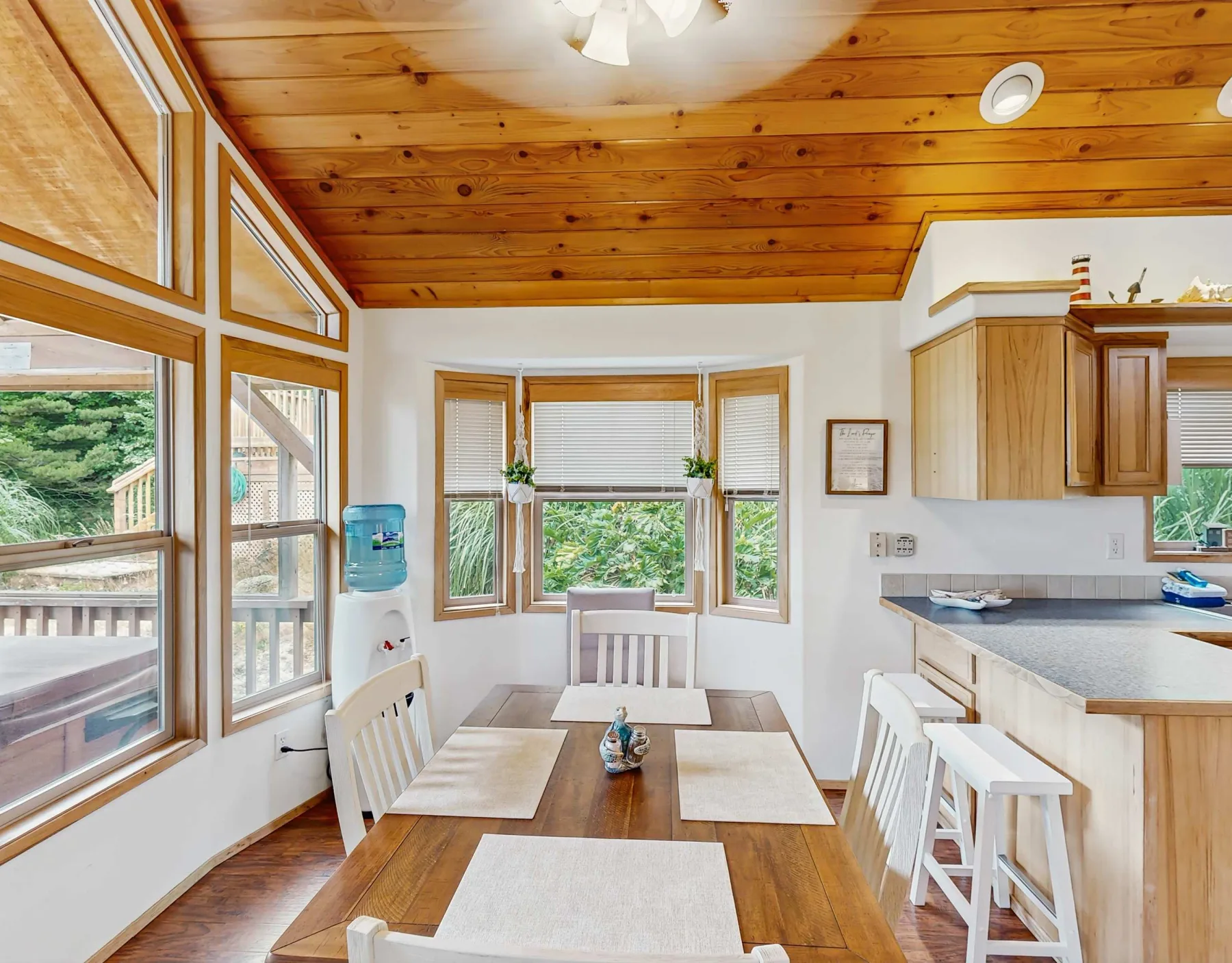 Un comedor luminoso con una mesa de madera junto a grandes ventanas y una encimera de cocina.