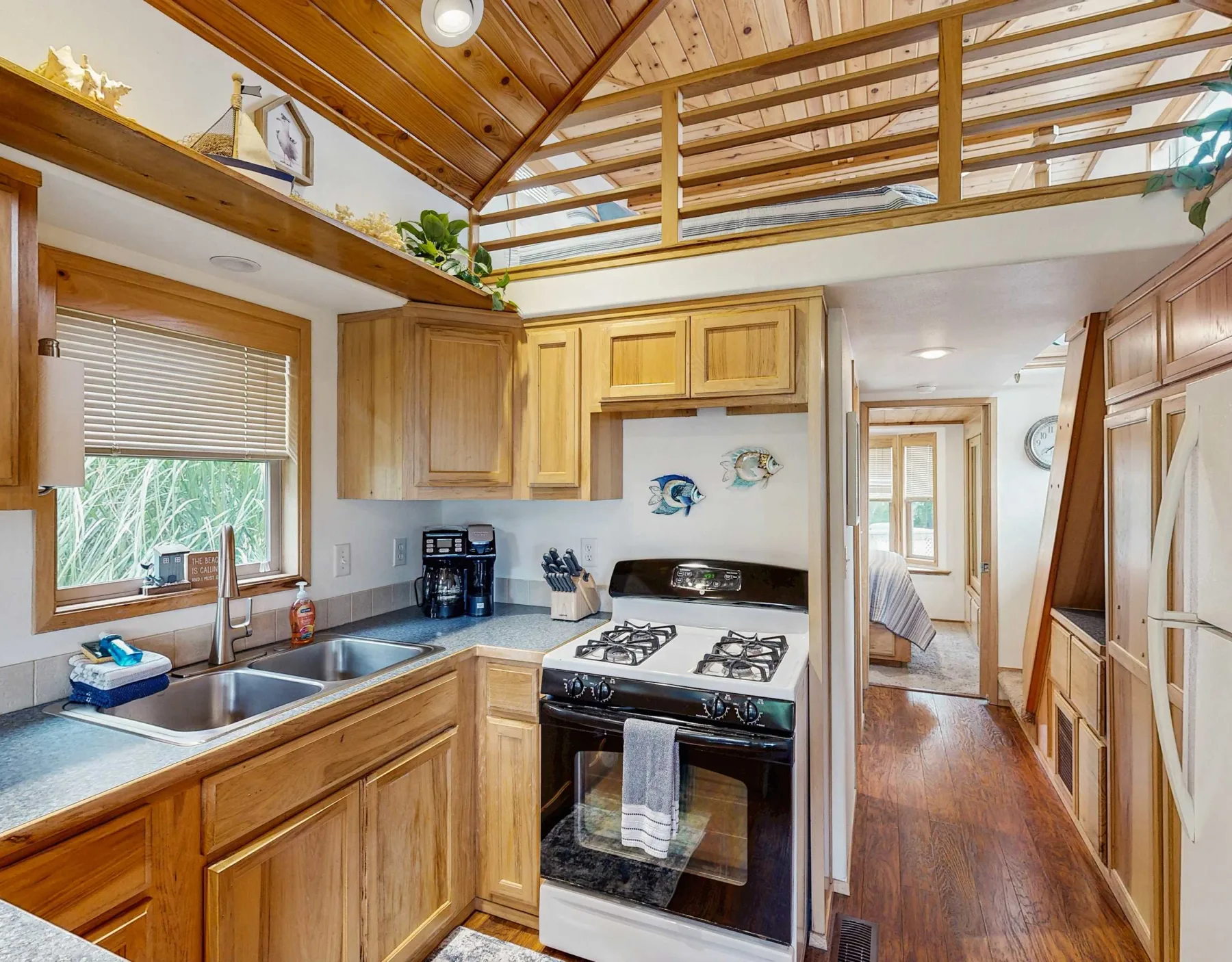 Una cocina revestida de madera con fregadero, estufa y gabinetes bajo una barandilla de altillo.
