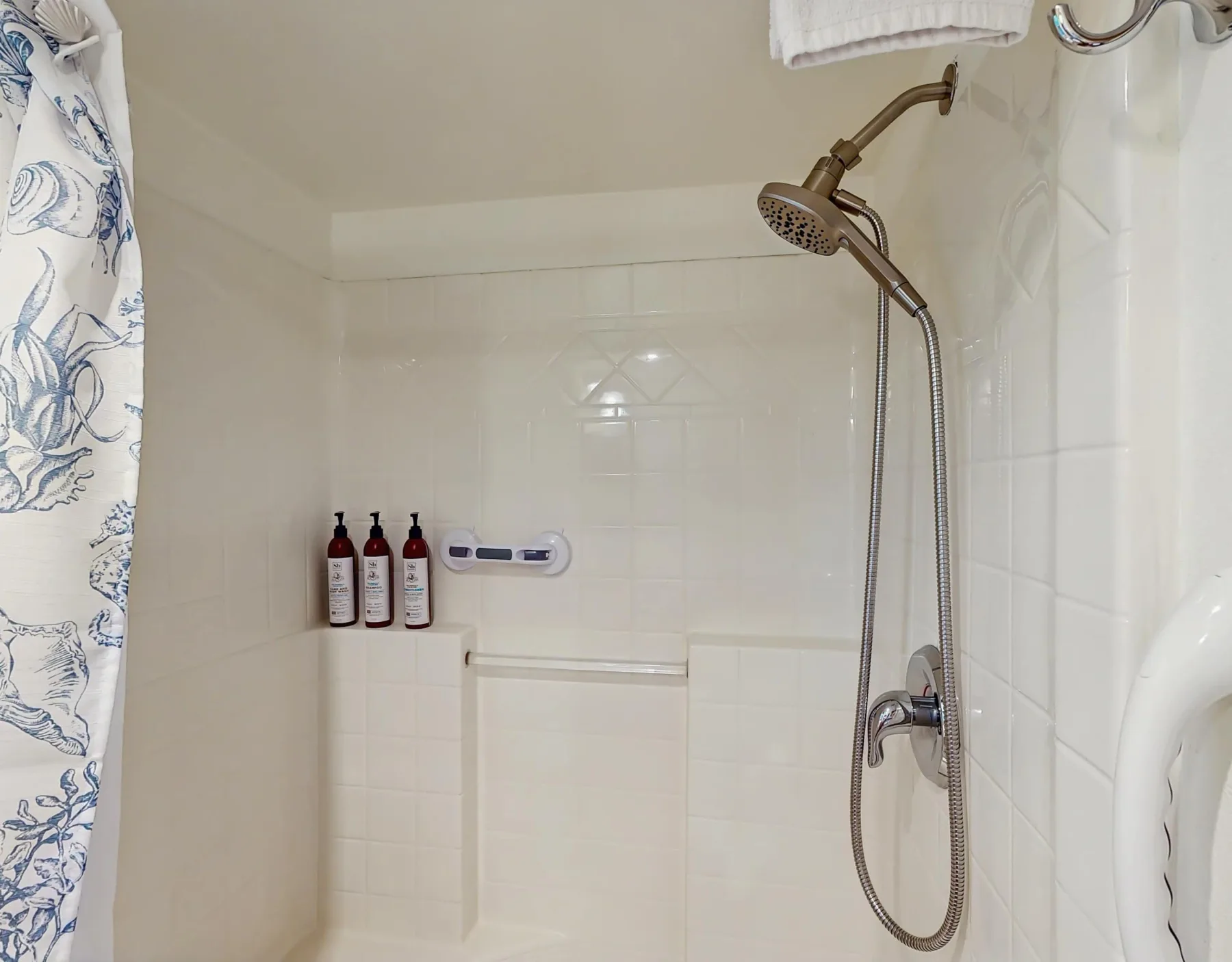 Una ducha de baño con azulejos, una ducha de mano y artículos de aseo en una repisa.