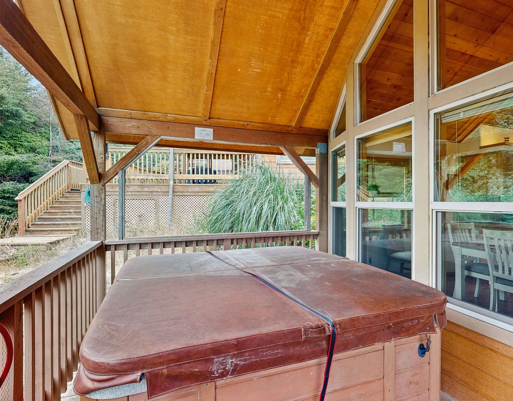 Una terraza de madera cubierta con una bañera de hidromasaje junto a grandes ventanas.