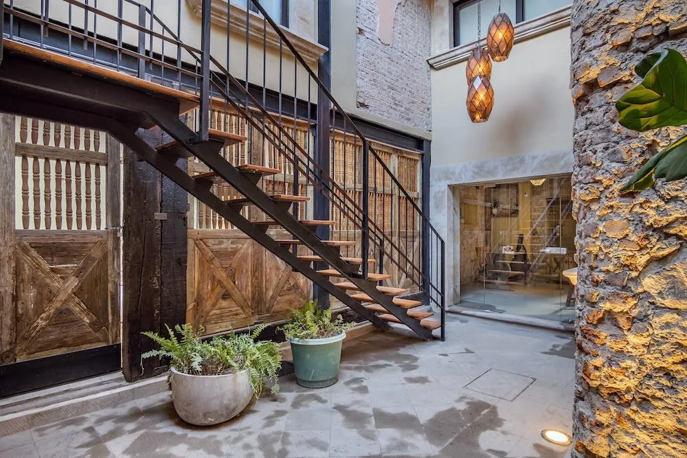 Zona común: Un patio interior con una escalera, plantas en macetas y una zona de estar acristalada.